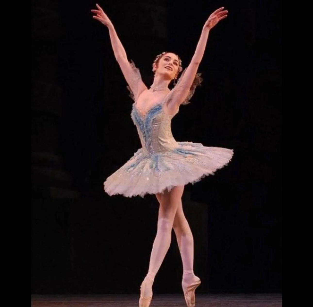 Victoria Hewitt in tutu performing on stage with arms raised and one leg slightly lifted.