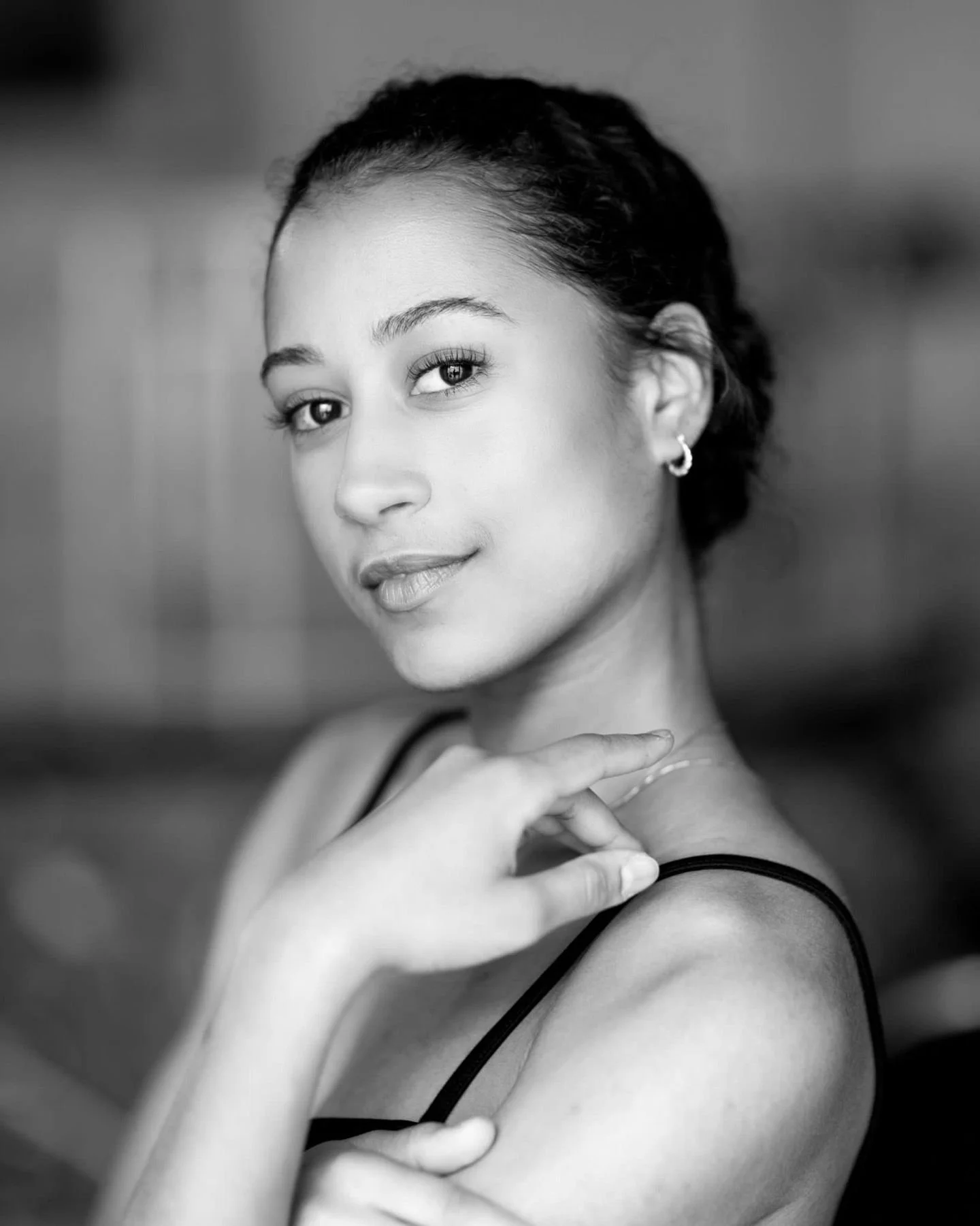Black and white portrait of a woman with short hair, wearing a sleeveless top, earrings, and looking at the camera with a slight smile.