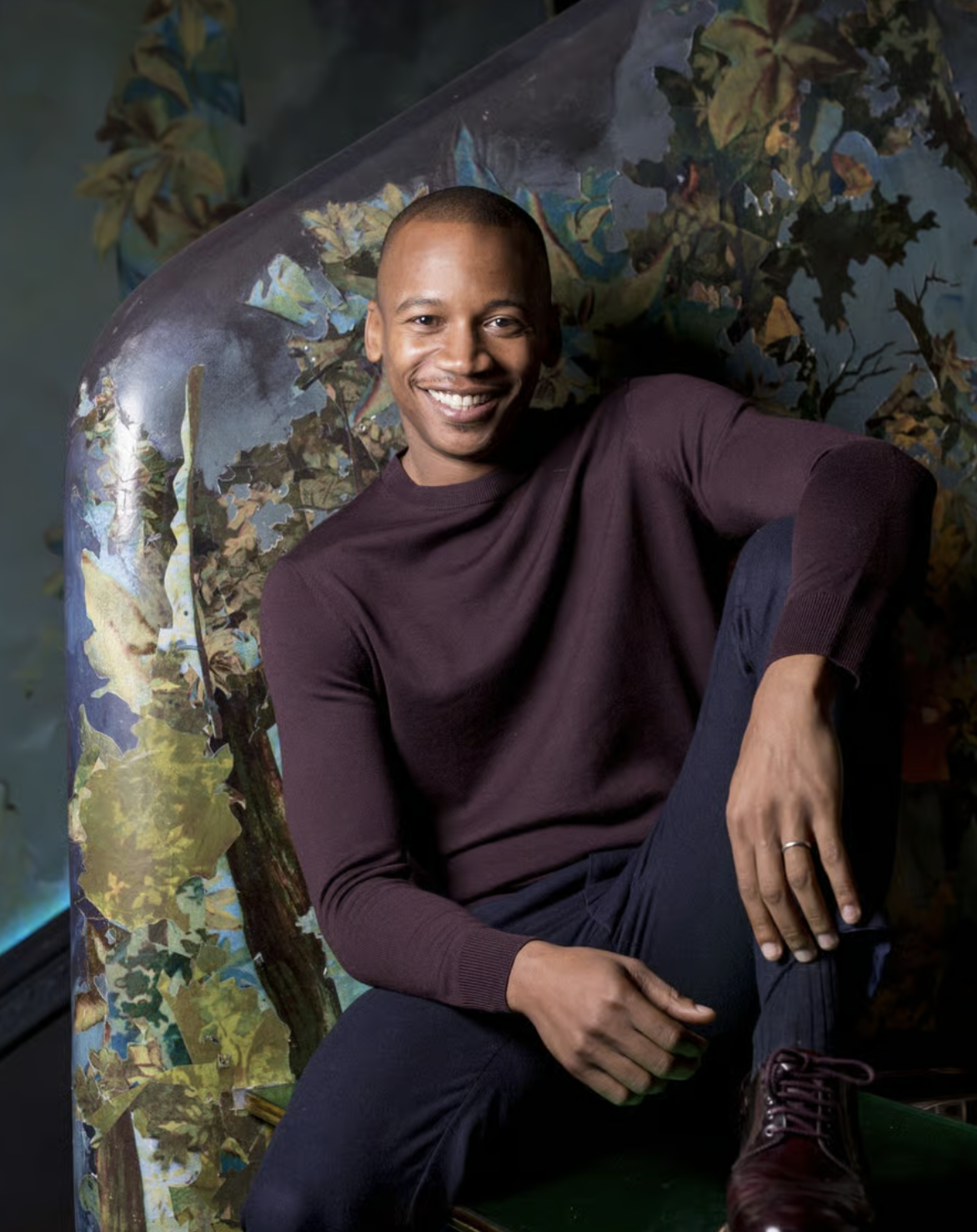 A picture of Eric Underwood, sitting on a dark green surface, with a colourful abstract background.