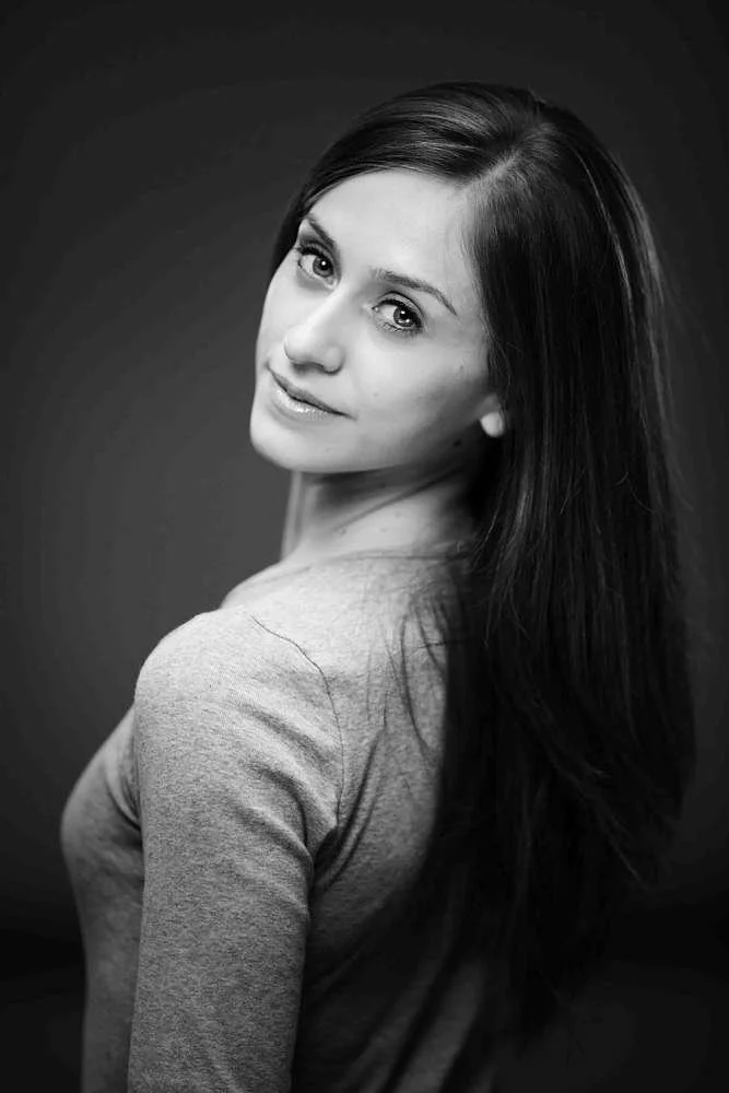 Black and white portrait of Marianela Nunez, looking over her shoulder with a slight smile, wearing a light-colored top.