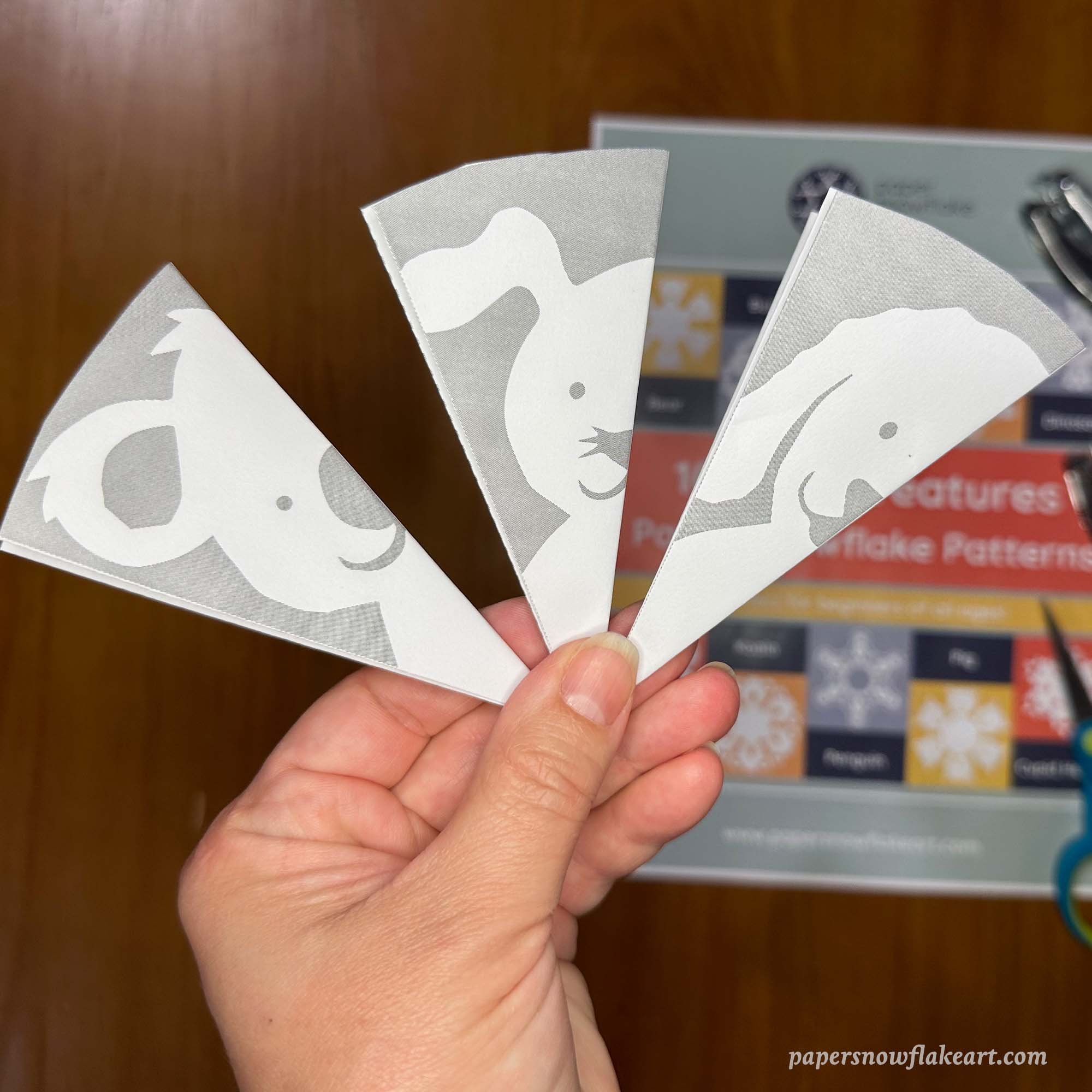 Hand holding three cute creature paper snowflake patterns
