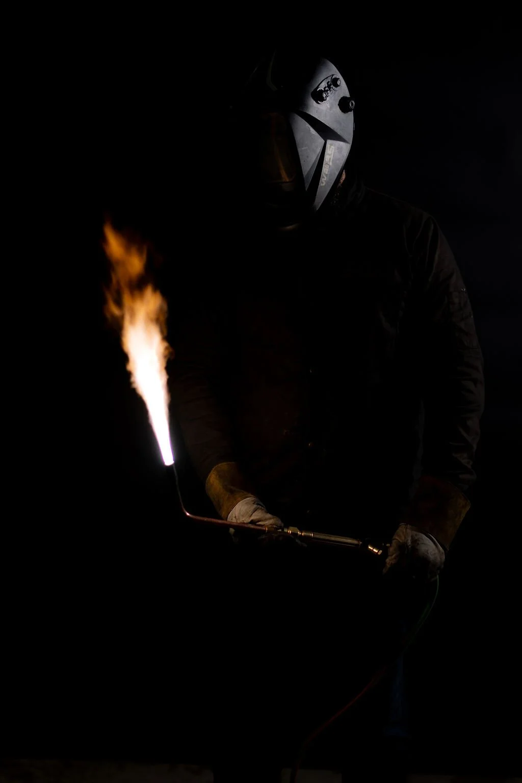 Welder in a black helmet holding a lit torch