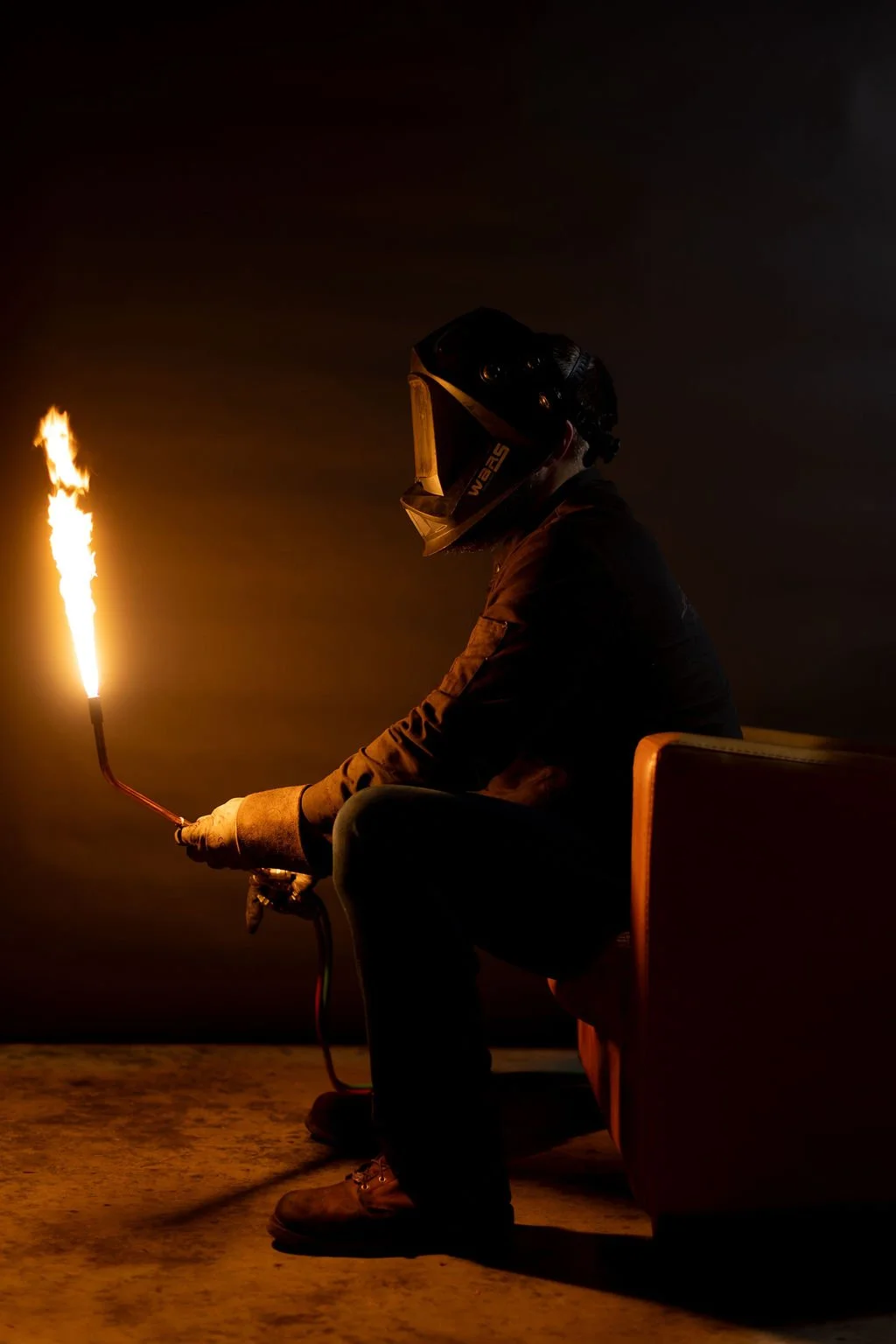A welder sitting in a leather chair holding a lit torch
