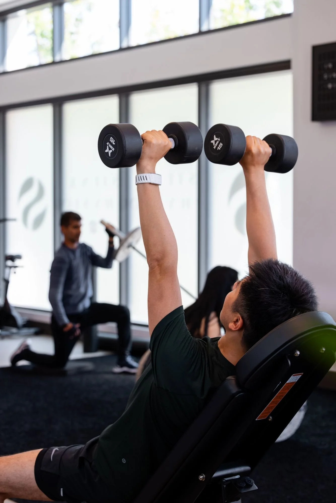 A member pressing dumbbells on an incline bench in a small group session