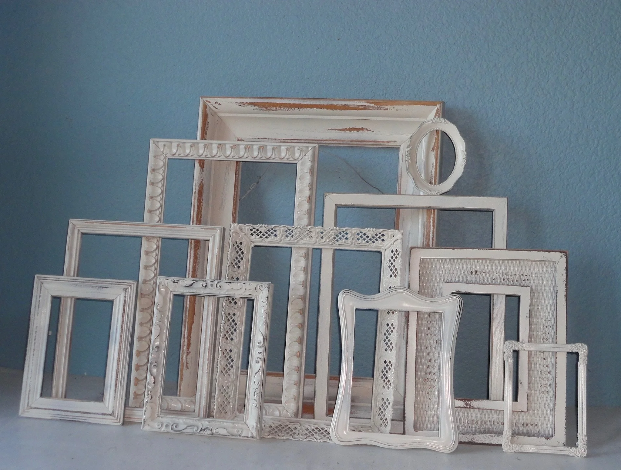 Arrangement of various empty vintage white picture frames leaning against a blue wall.