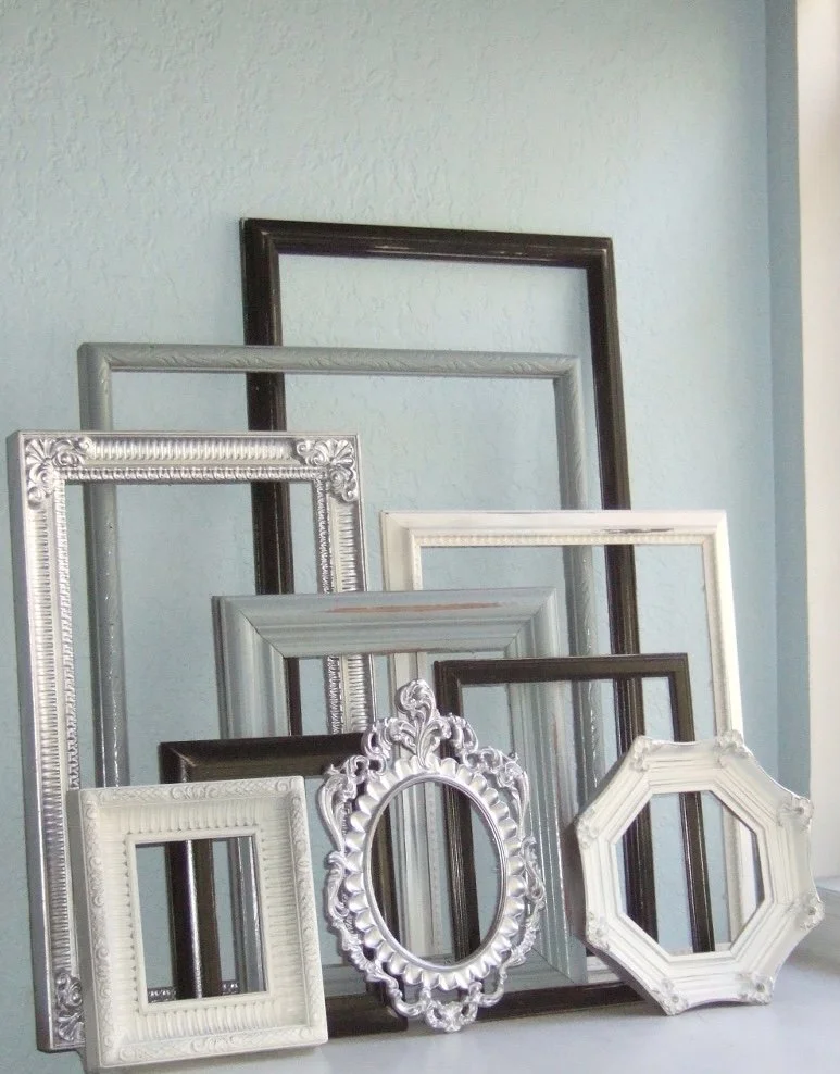 Several empty decorative picture frames in various shapes and sizes lean against a light blue wall.