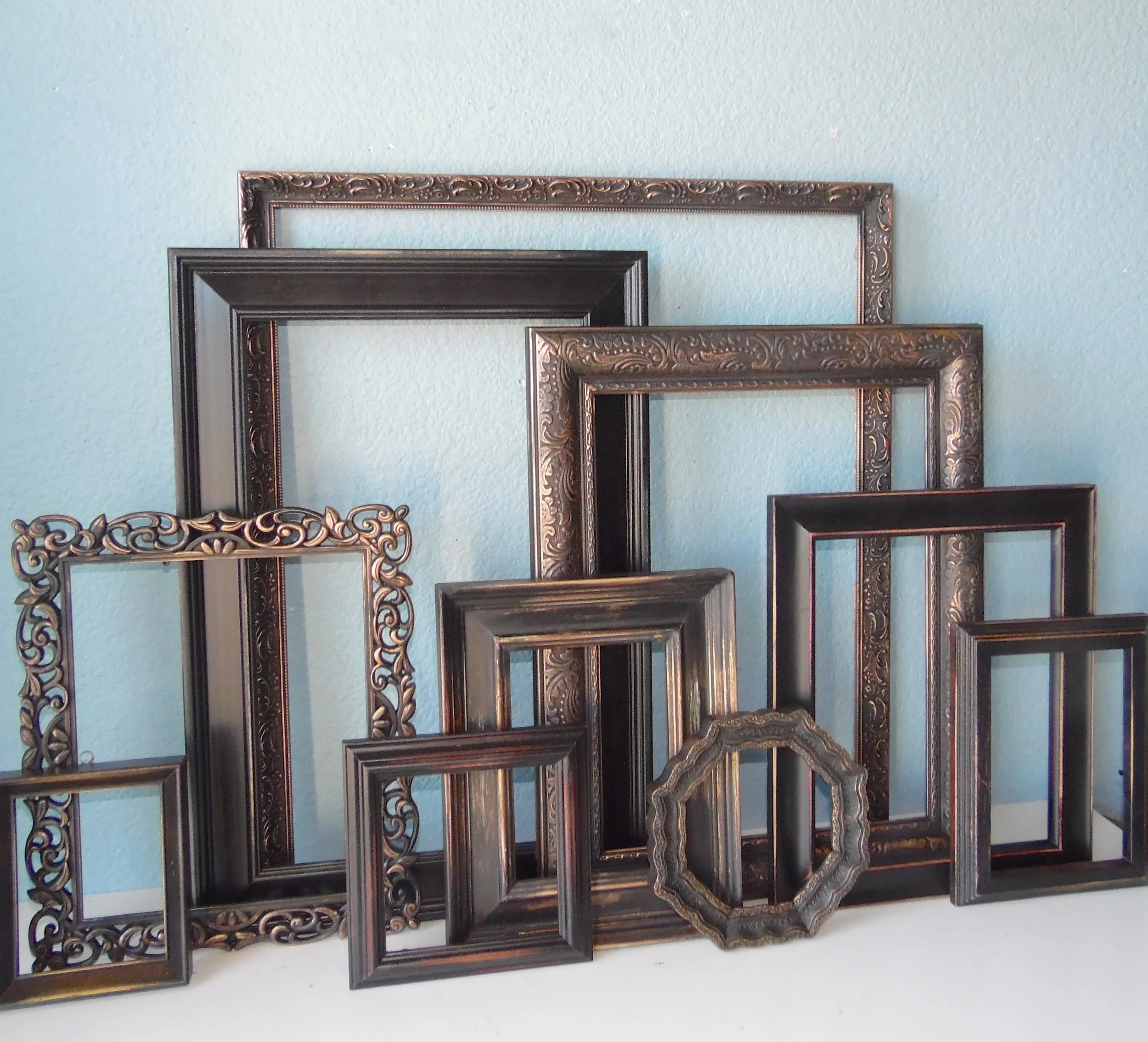 Multiple empty decorative picture frames in various sizes and styles leaning against a light blue wall.