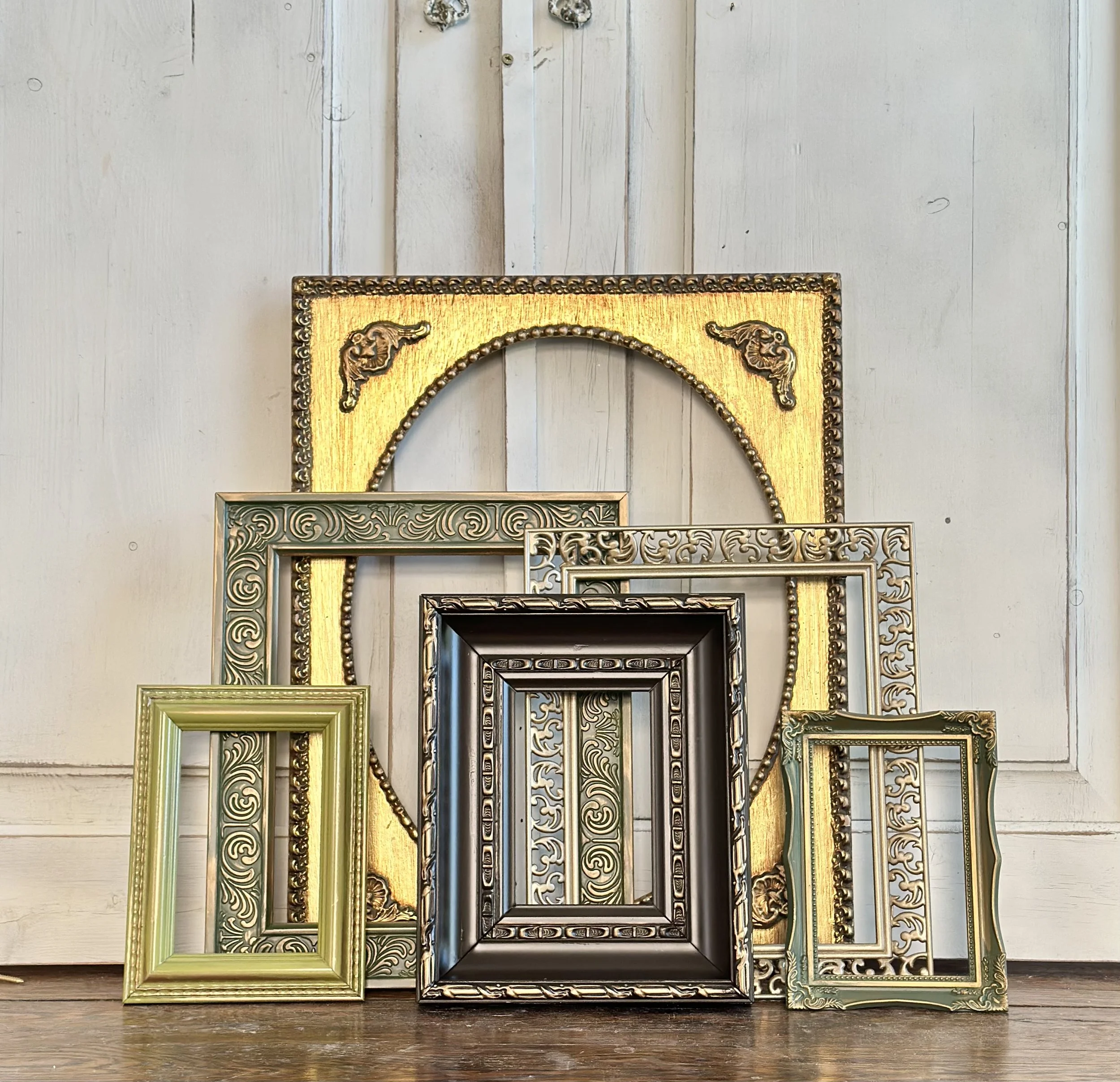 Various ornate picture frames in different sizes and colors, arranged in front of a white wooden door.