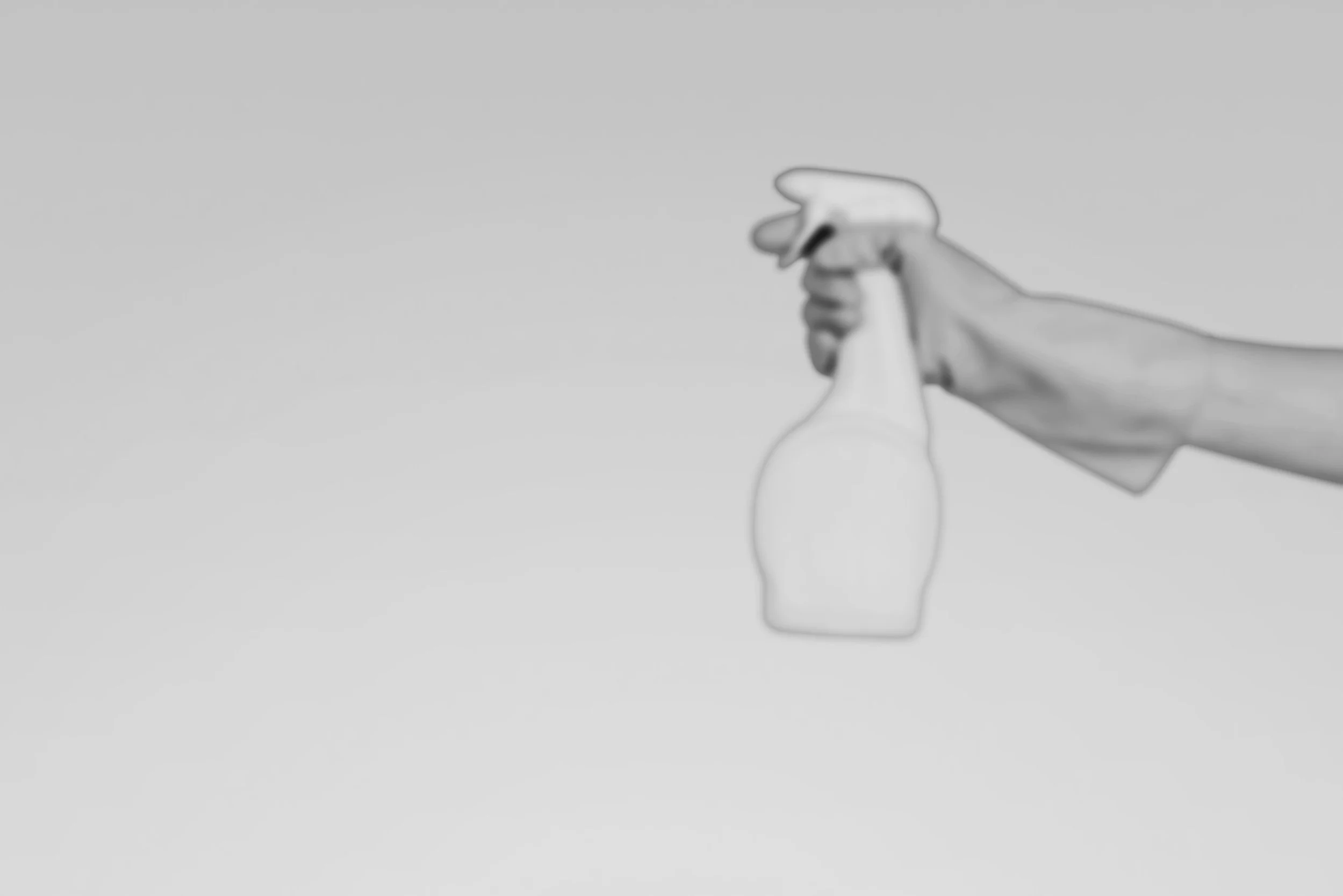 A person wearing white gloves is holding a spray bottle, and pointing it to the right.