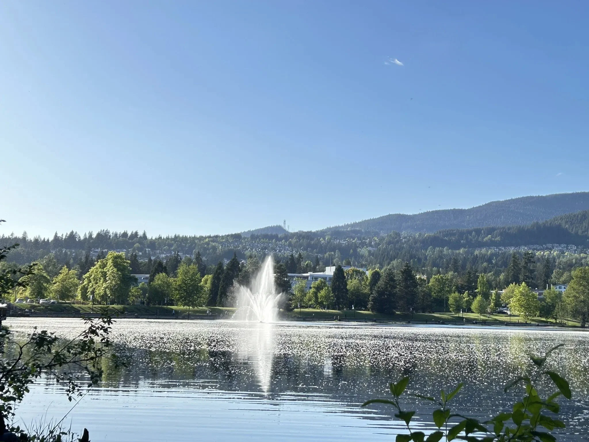 Coquitlam's Lafarge Lake with a fountain, reflecting mountains and blue sky, symbolizing outdoor leisure.
