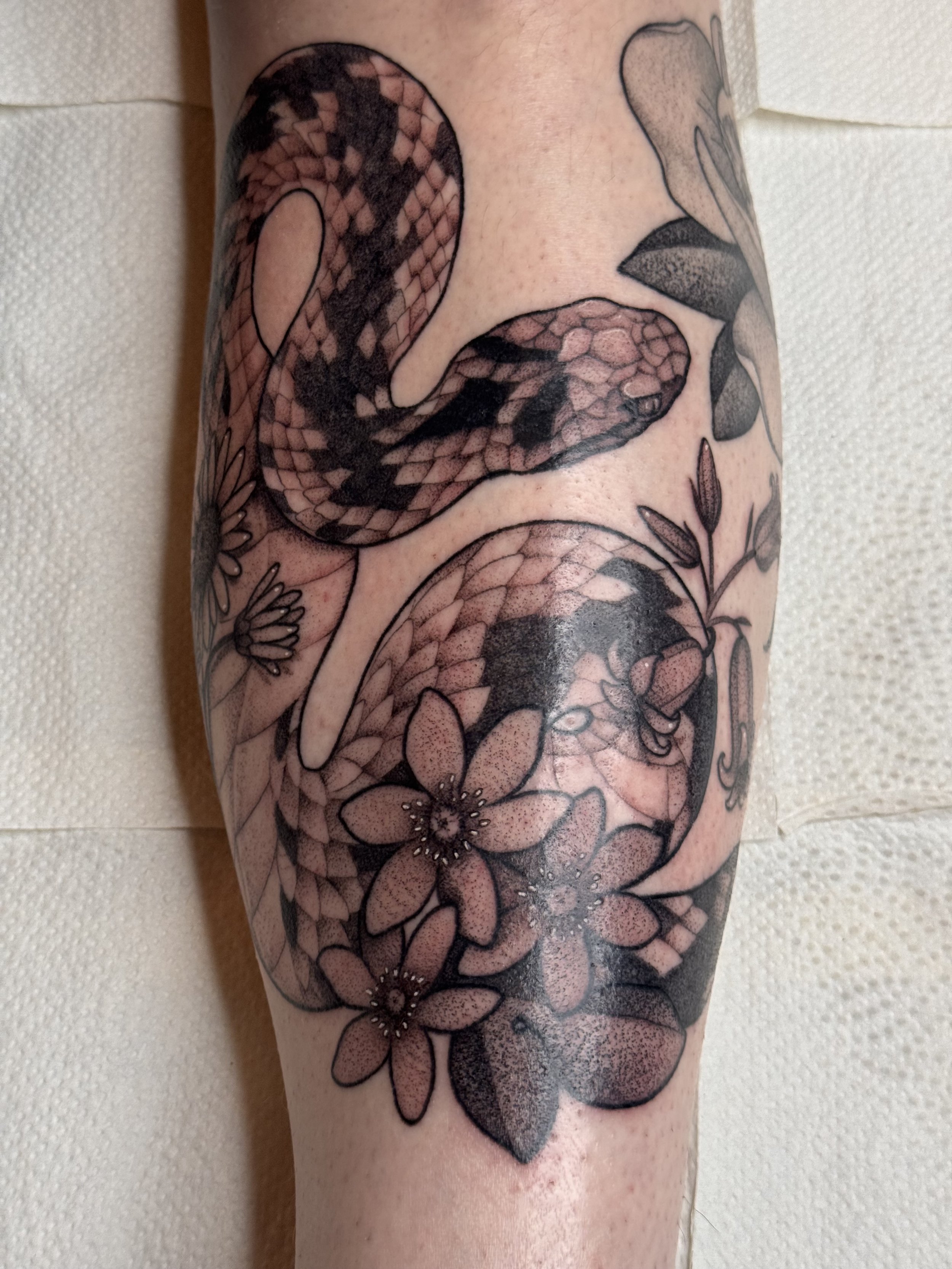 Viper snake tattoo on shin with flowers