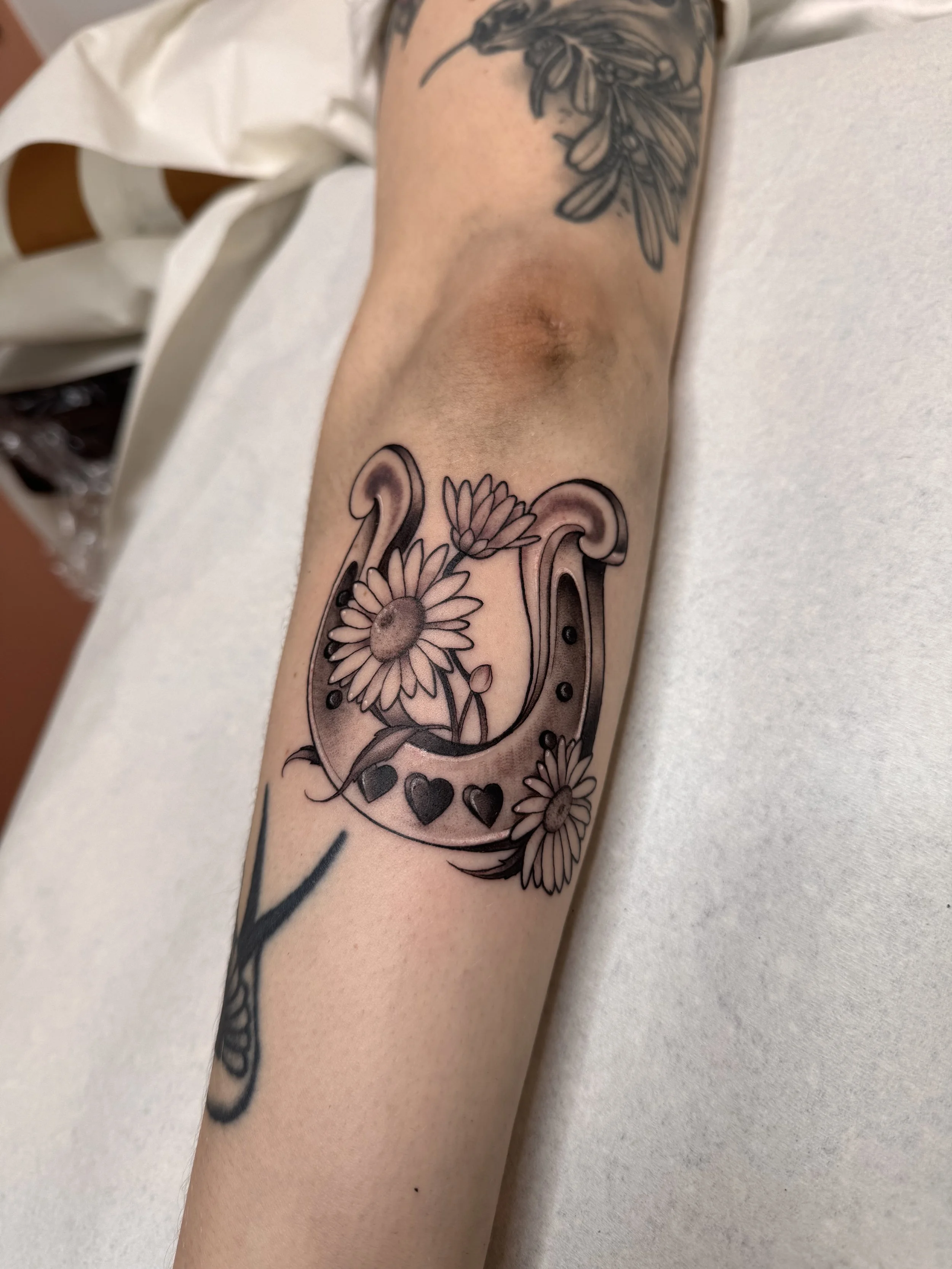 Neotraditional tattoo of a horseshoe in black and grey smooth shading with daisies