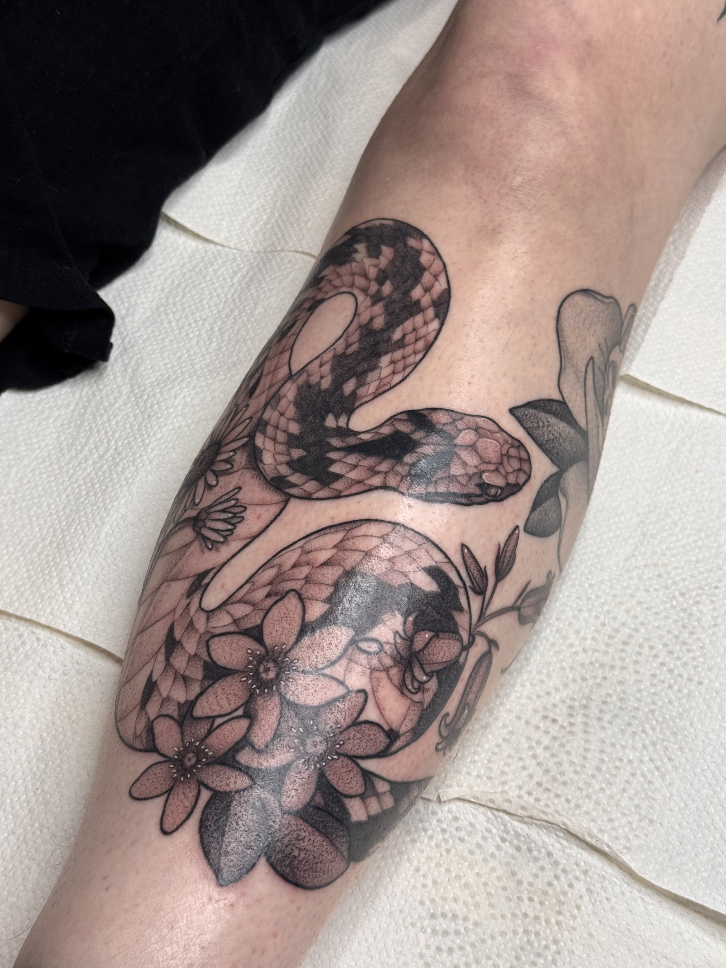 Viper snake tattoo on shin with flowers