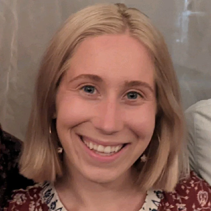 Close-up of a smiling woman with shoulder-length blonde hair, blue eyes, and wearing patterned clothing.