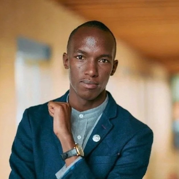 A young man with short hair, wearing a blue blazer and light-colored shirt, posing indoors with a neutral background.