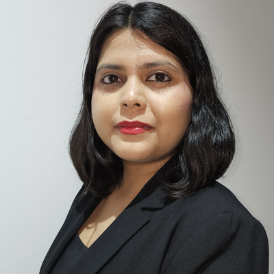 A woman with shoulder-length black hair, wearing a black blazer, looking at the camera against a plain gray background.
