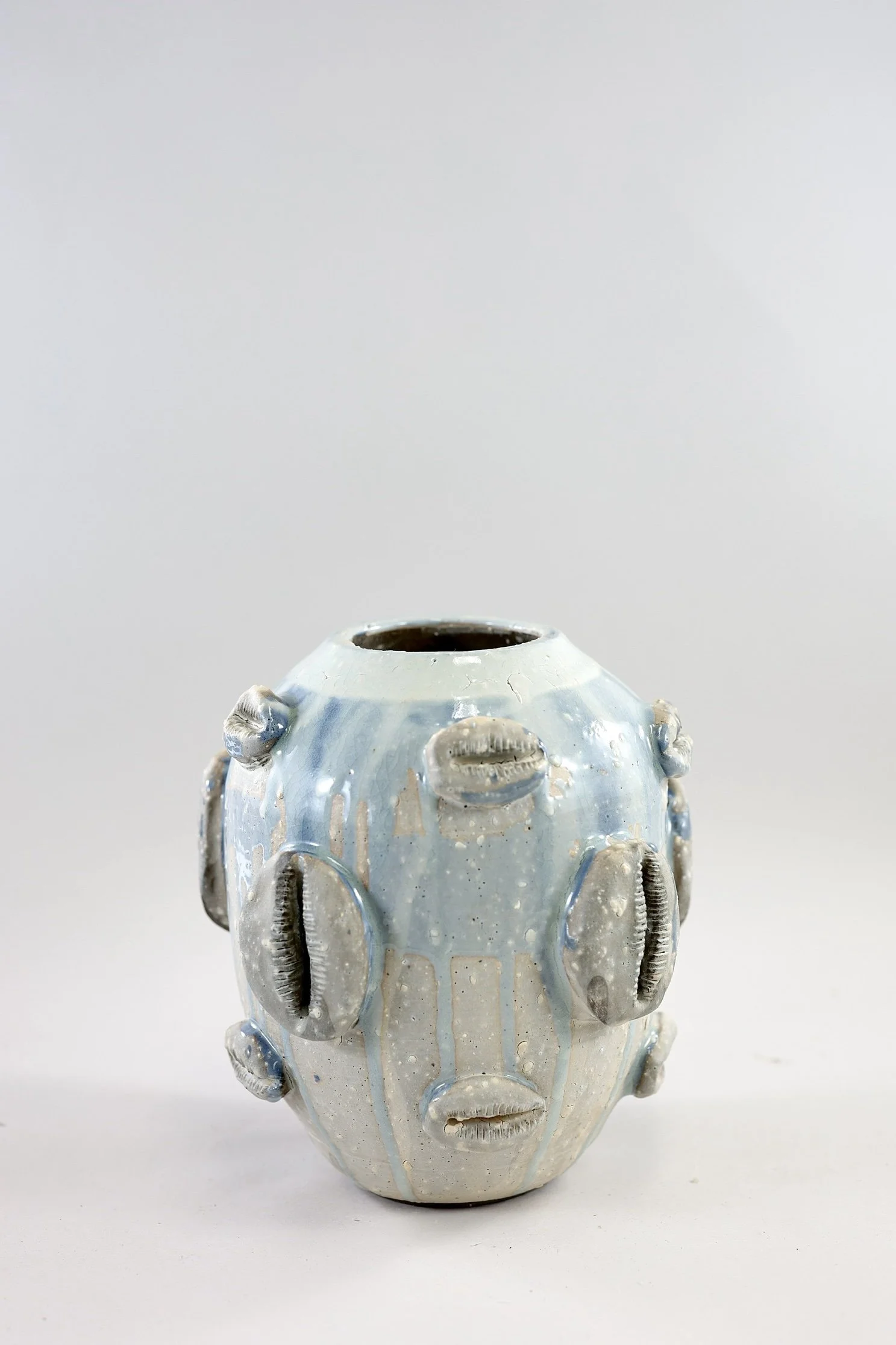 stoneware vessel with a dripping blue glaze with sculpted cowrie shells around it