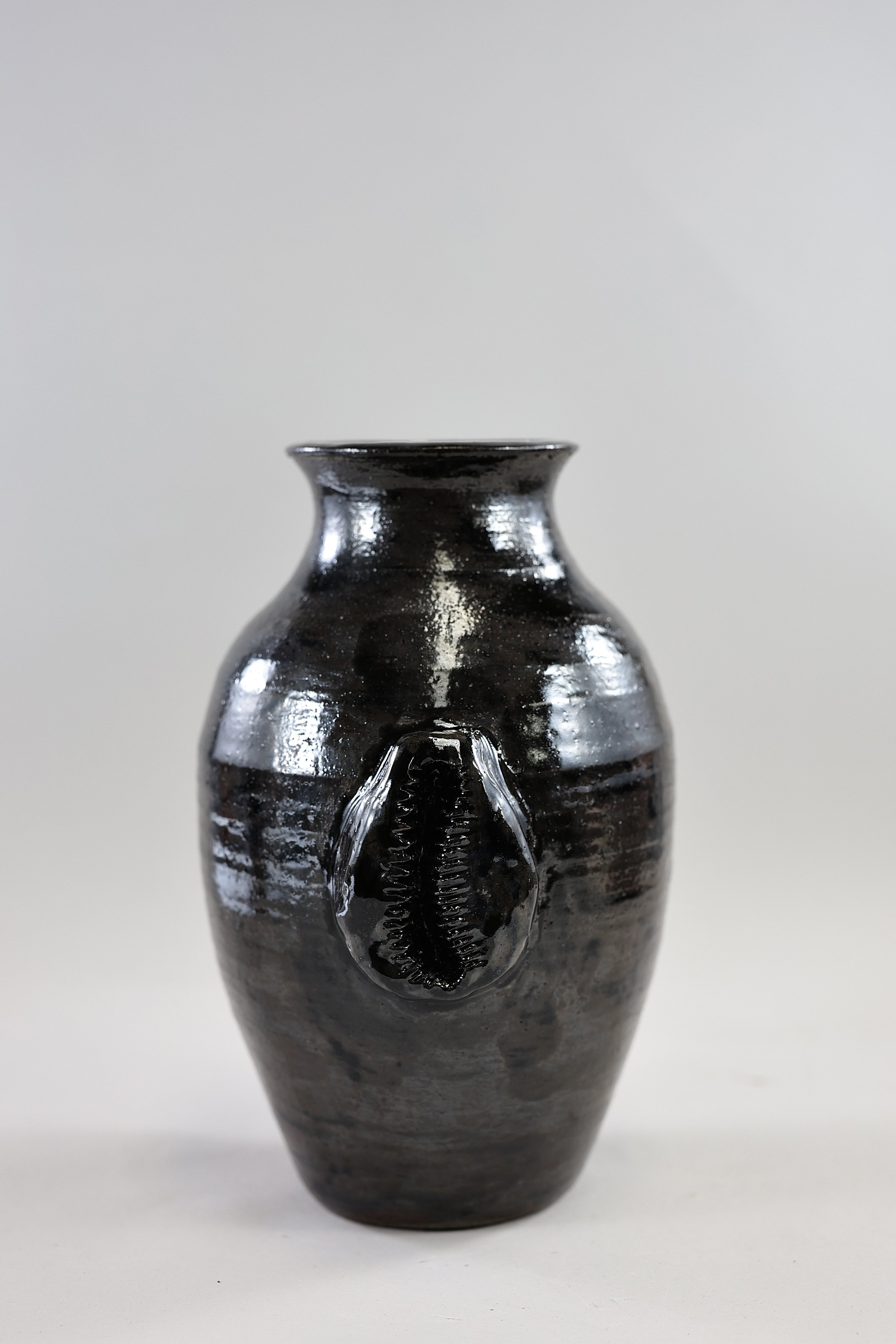 Shiny black stoneware vessel with large ceramic cowrie shell in the middle