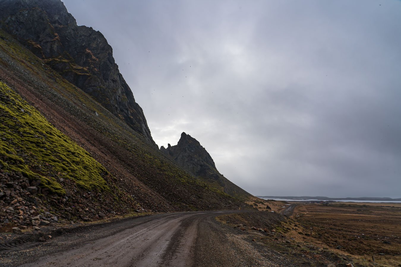  The dirt road leading to  Vestrahorn  offers stunning views of the surrounding cliffs and mossy slopes, giving a taste of the scenery before reaching the iconic mountain. 