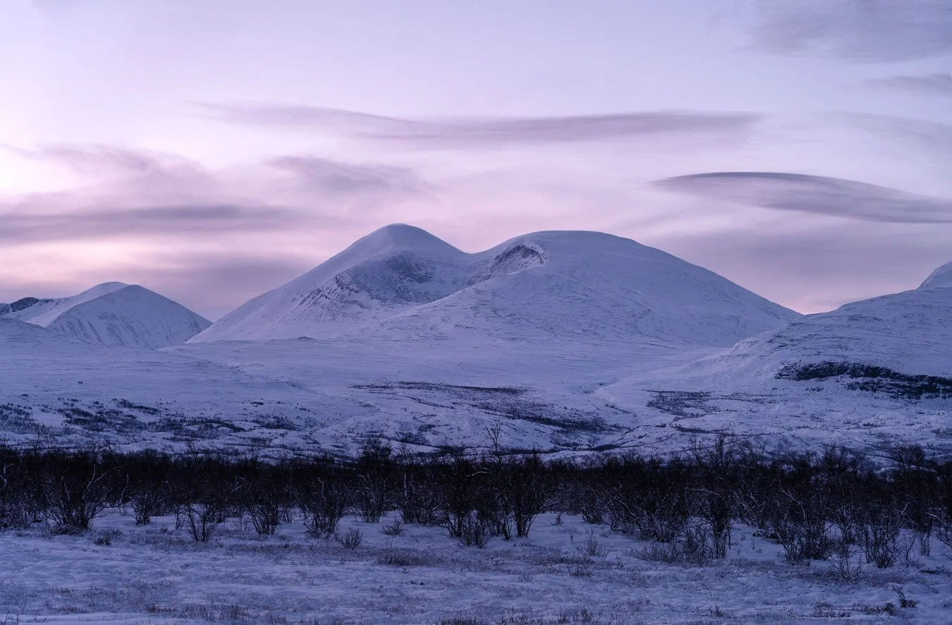 Snow-covered mountain in Abisko National Park, Swedish Lapland, softly illuminated by faint pink and purple light during polar dawn in winter.
