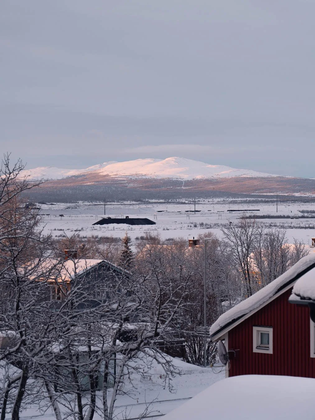 Sunrise view of a snow-covered hill near Kiruna, Sweden, captured with a telephoto lens highlighting the soft morning light over the surrounding landscape.