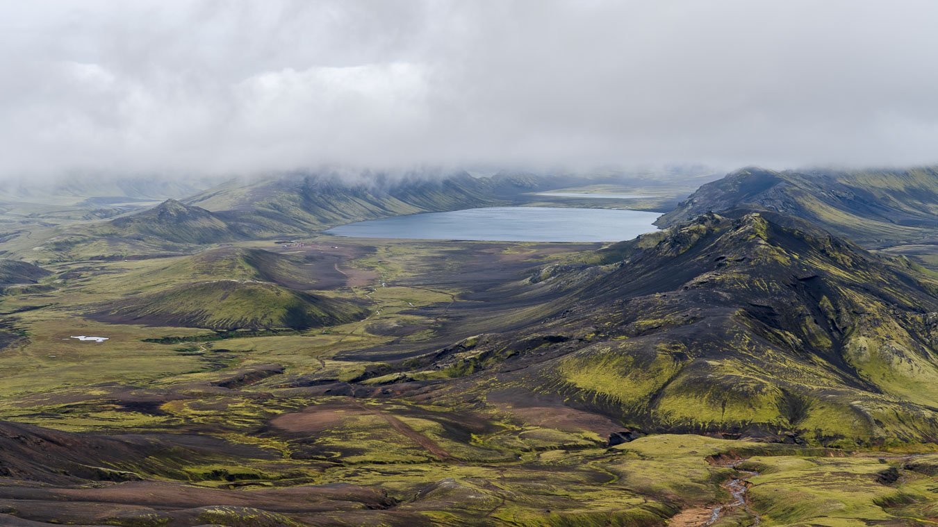 View over Lake Álftavatn from the steep ascent toward Hrafntinnusker on the Laugavegur trail in Iceland, with expansive highland scenery slightly obstructed due to cloudy conditions..