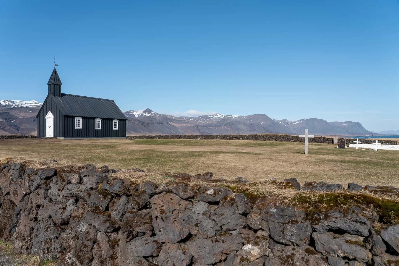 Búðakirkja, the historic black church on Snæfellsnes Peninsula, surrounded by lava fields and distant mountains under a clear blue sky.