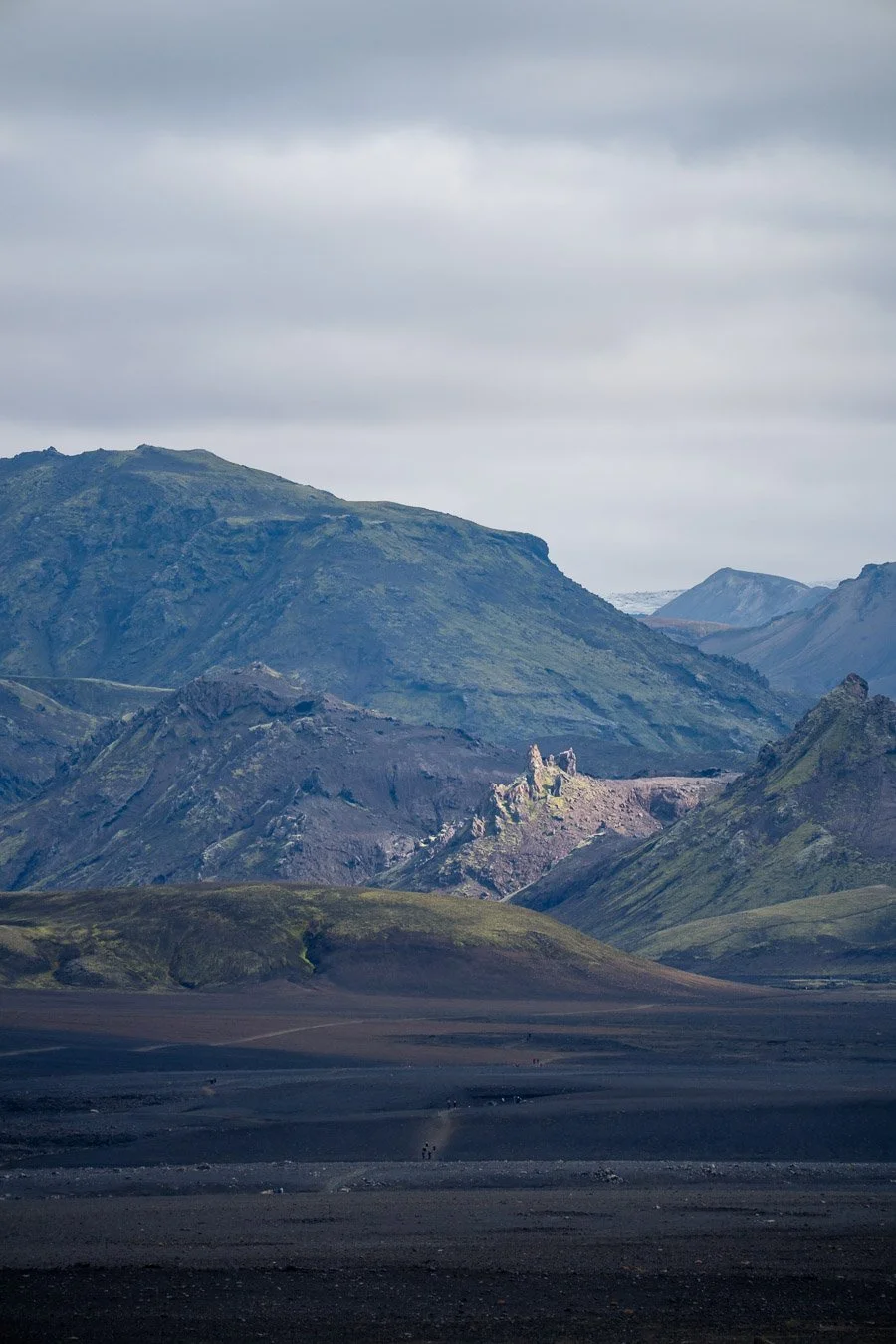 Dramatic view across the black sand desert on the Laugavegur trail between Emstrur and Álftavatn/Hvanngil in Iceland’s Highlands, with rugged mountains in the distance under striking light.
