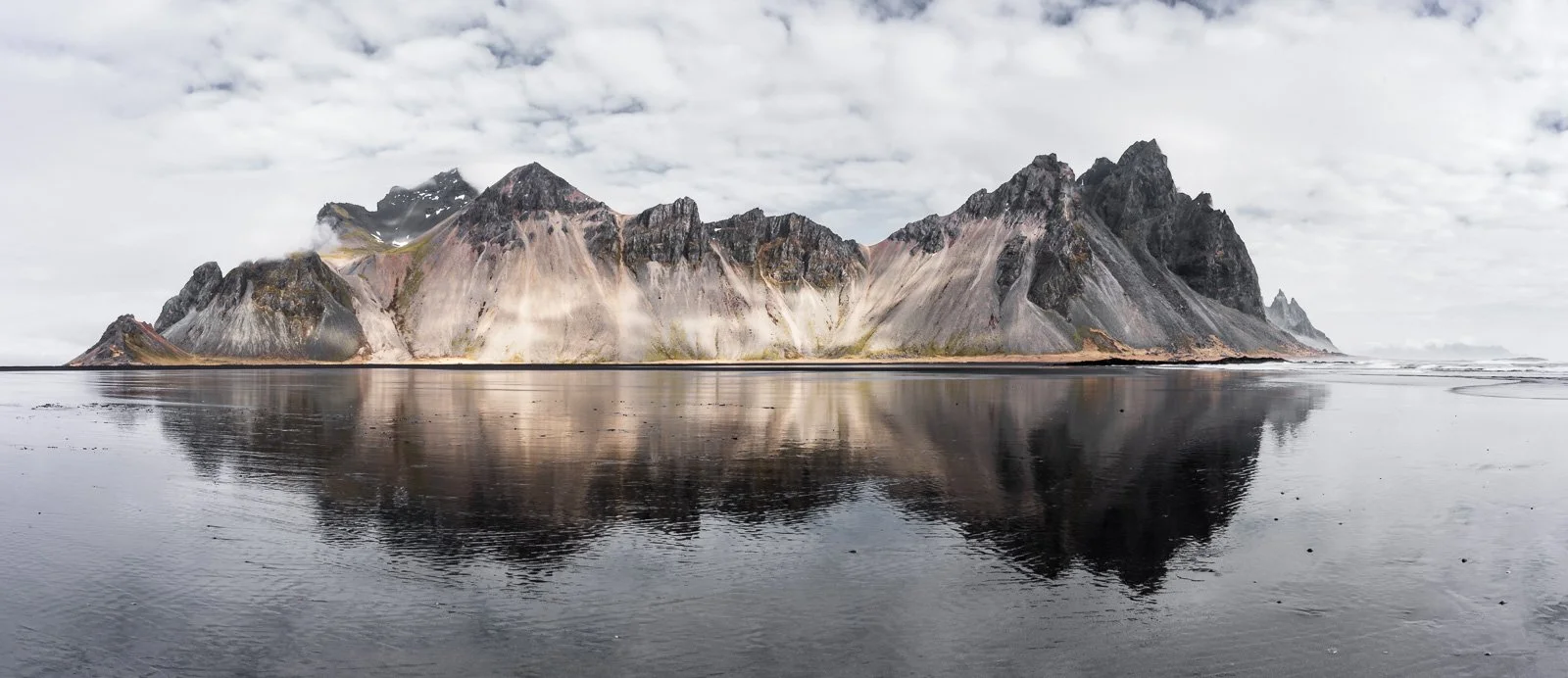 Reflection of the dramatic Vestrahorn mountain range on a black sand beach, creating a striking mirror-like effect.