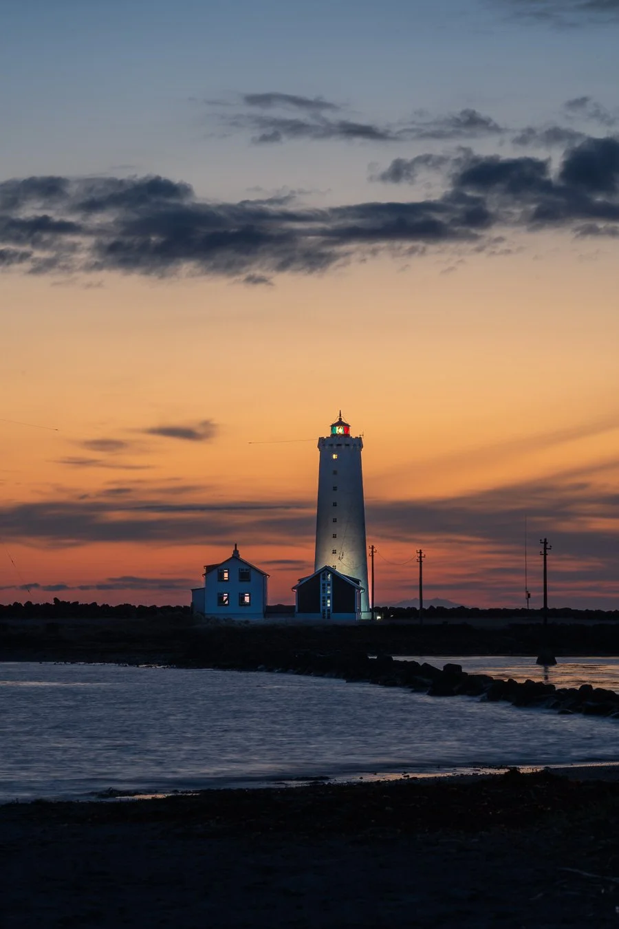 Grótta Lighthouse on Grótta Island near Reykjavík, illuminated at sunset with a glowing orange and blue sky.