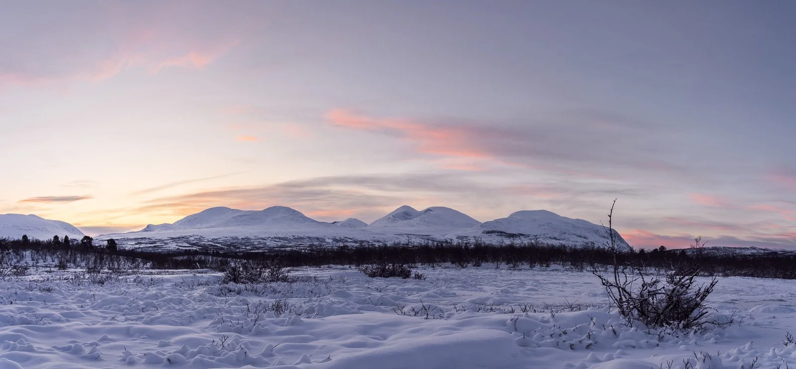 Snow-covered mountains beneath glowing red clouds at winter sunrise, seen from the Njullá nature trail in Abisko National Park, Swedish Lapland, northern Sweden.