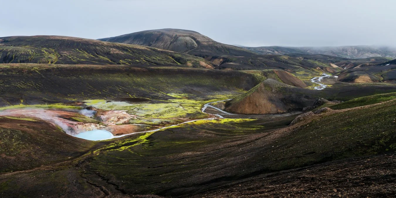 View of the Hamragilskvísl stream in Iceland’s Highlands, winding through intensely colored moss and flowing into a vivid turquoise hot pool along the Laugavegur trail.