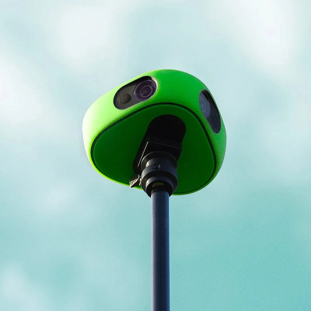 Close-up of a green Veo camera and sensor components, viewed from below against a cloudy sky.