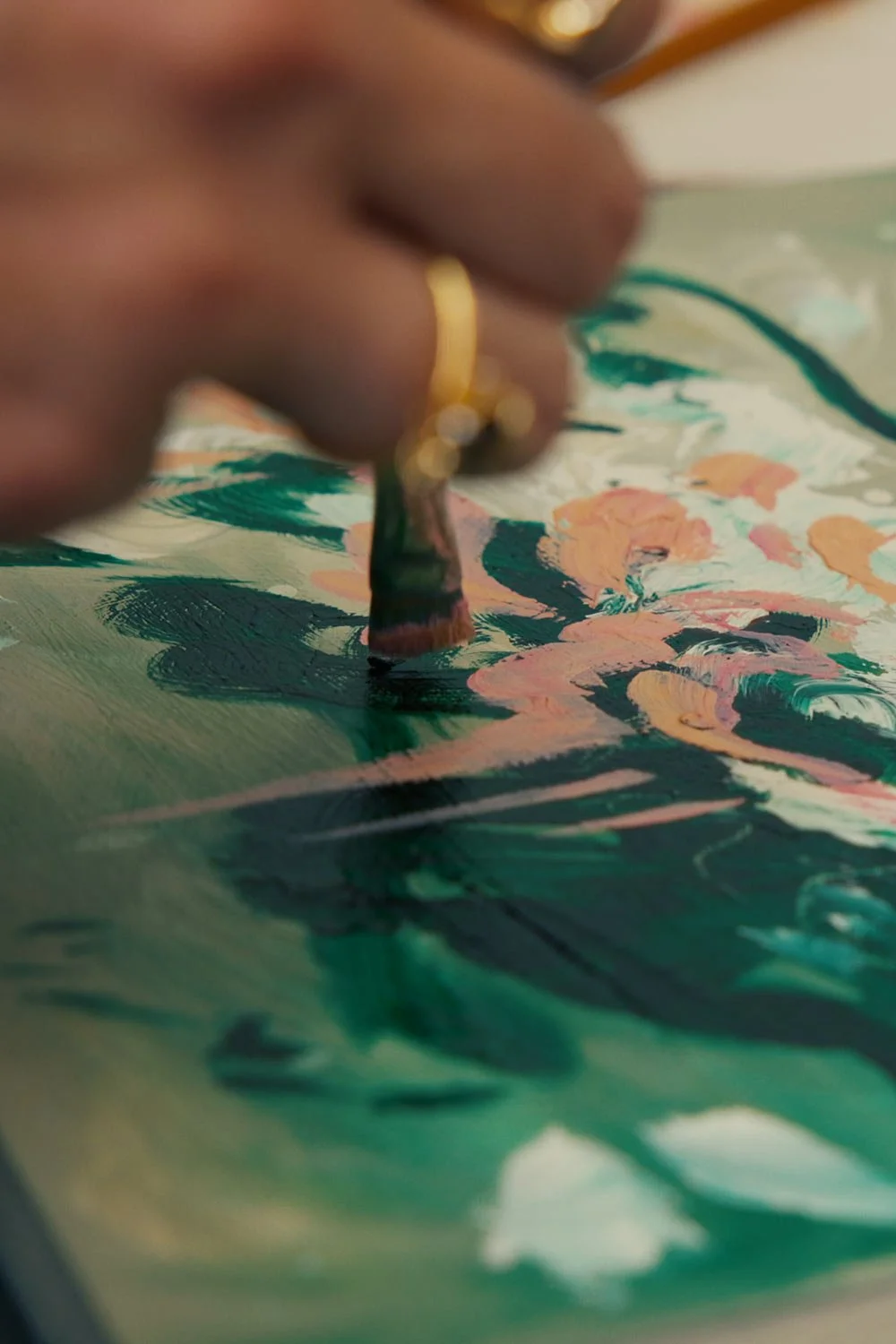 Close-up of a person, Ramona Armitage, painting on canvas with small brush, creating a colourful floral scene with pink, peach, green, and dark shades.