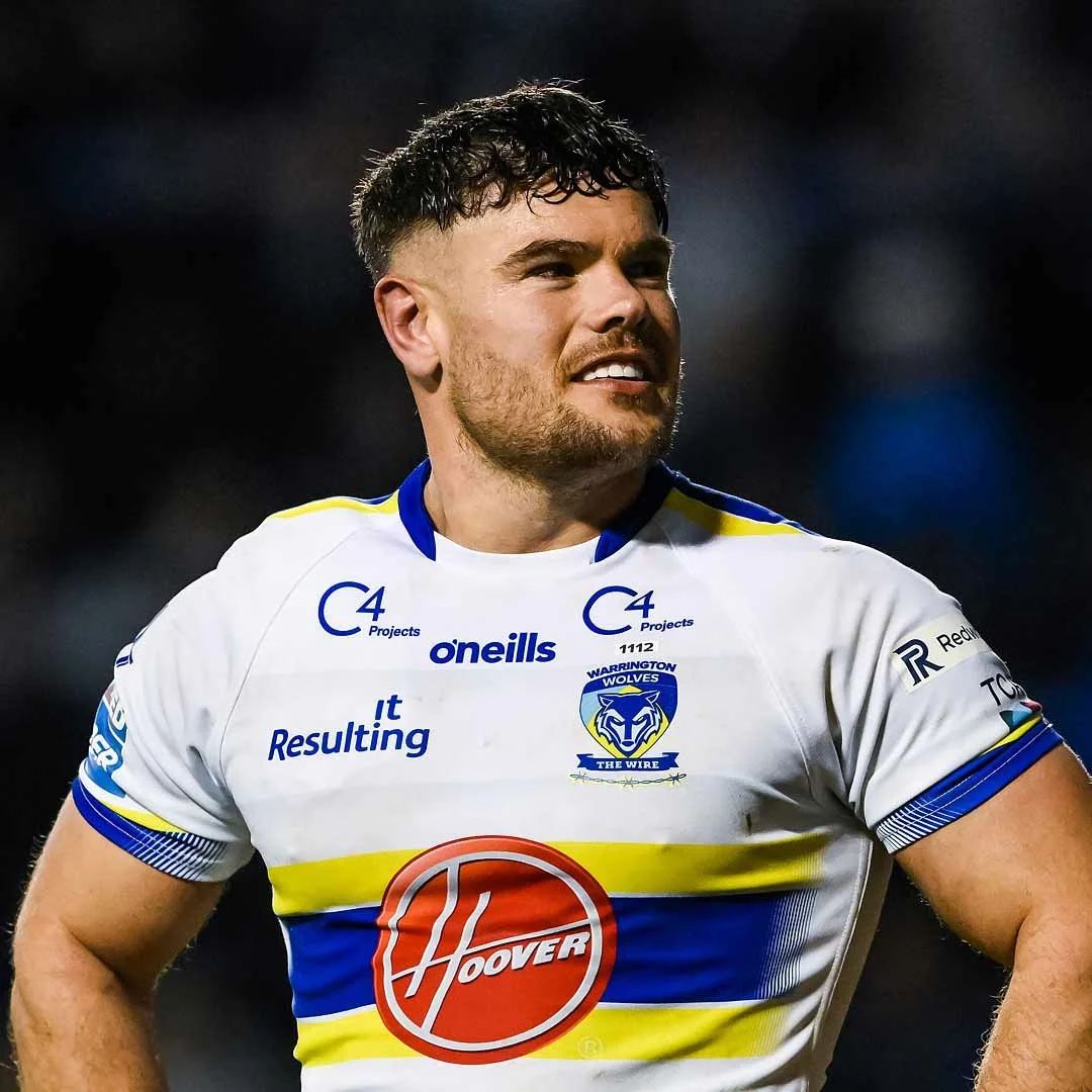 A male rugby player, Joe Philbin, in a Warrington Wolves team jersey with sponsor logos, standing outdoors.
