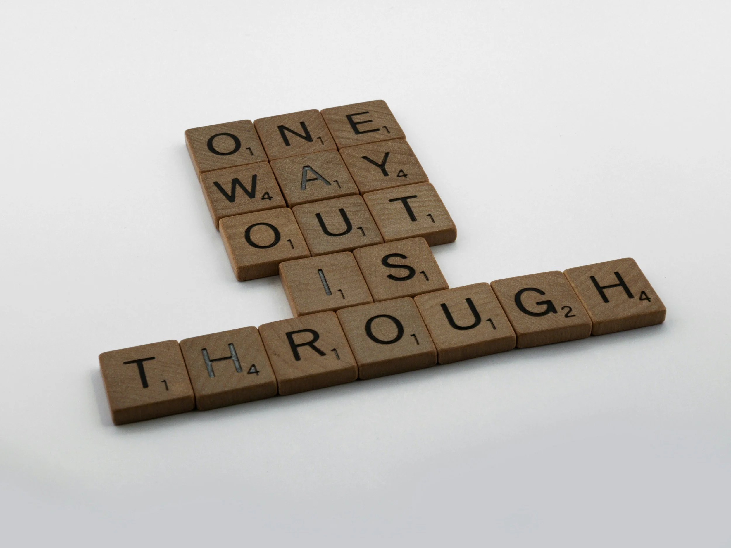 Wooden Scrabble tiles spelling "ONE WAY OUT" on a white background.