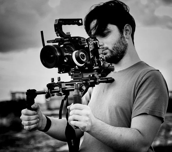 Man operating a professional video camera on a shoulder rig outdoors in black and white.