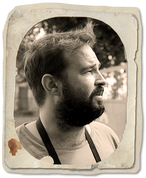 Black and white photo of a bearded man with short hair looking to the right, with a torn and stained vintage-style paper border.