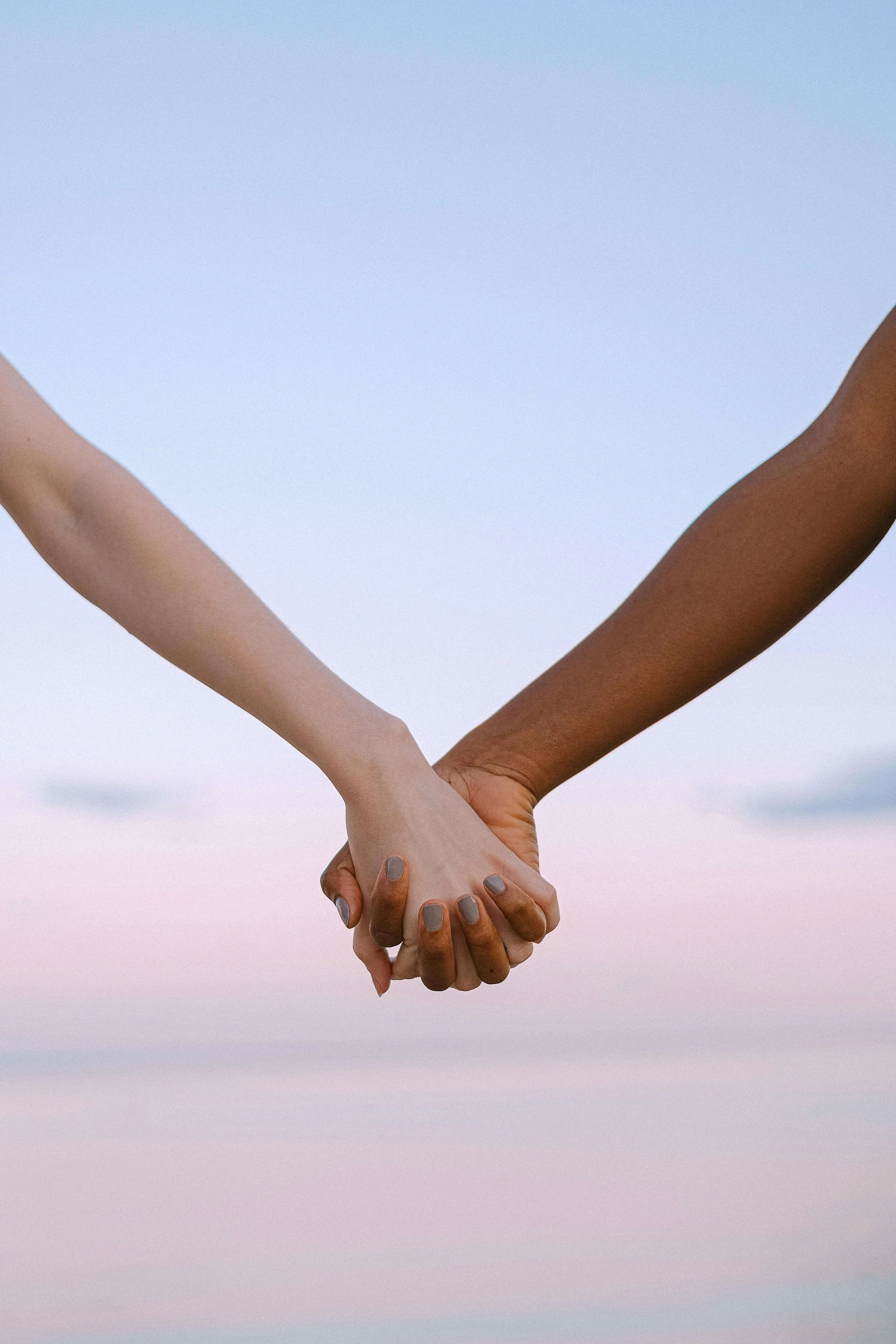 Two people holding hands against a pastel sky background.