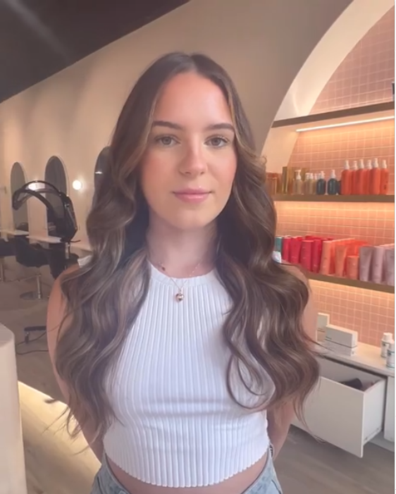 A young woman with long, wavy brown hair standing in a salon