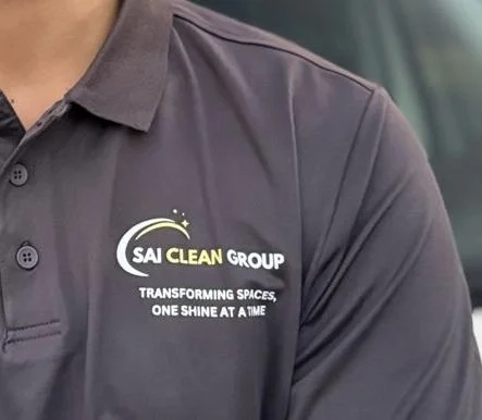 Close-up of a person wearing a dark gray polo shirt with the SAI CLEAN GROUP logo and slogan on the chest.