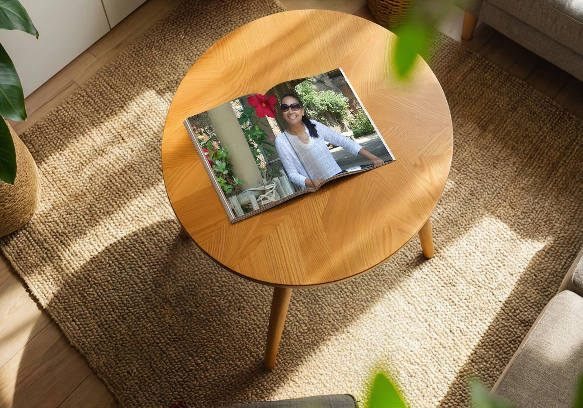 Open photo album on a round wooden coffee table in a cozy room with a beige textured rug. The album shows a woman with sunglasses smiling outdoors among plants and a stone wall.