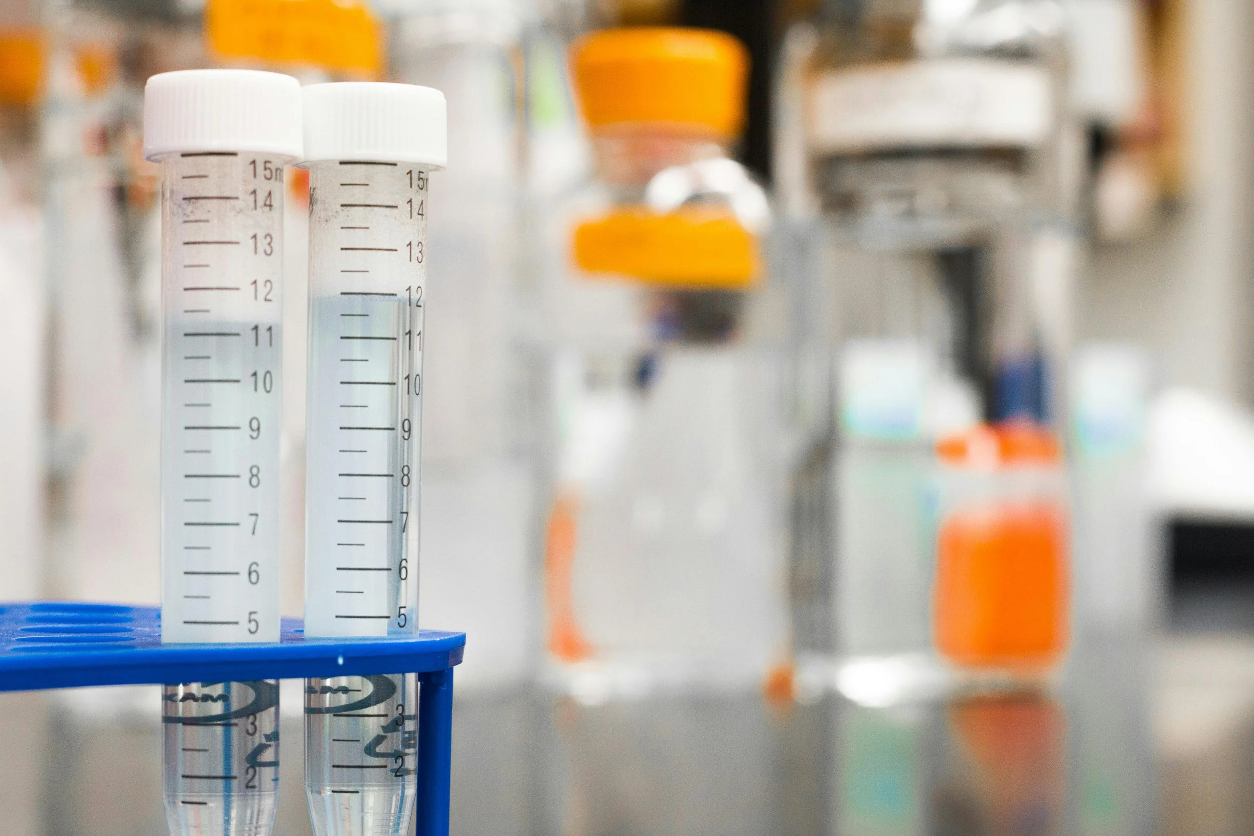 Laboratory test tubes in a rack with a blurred background of laboratory supplies and equipment.