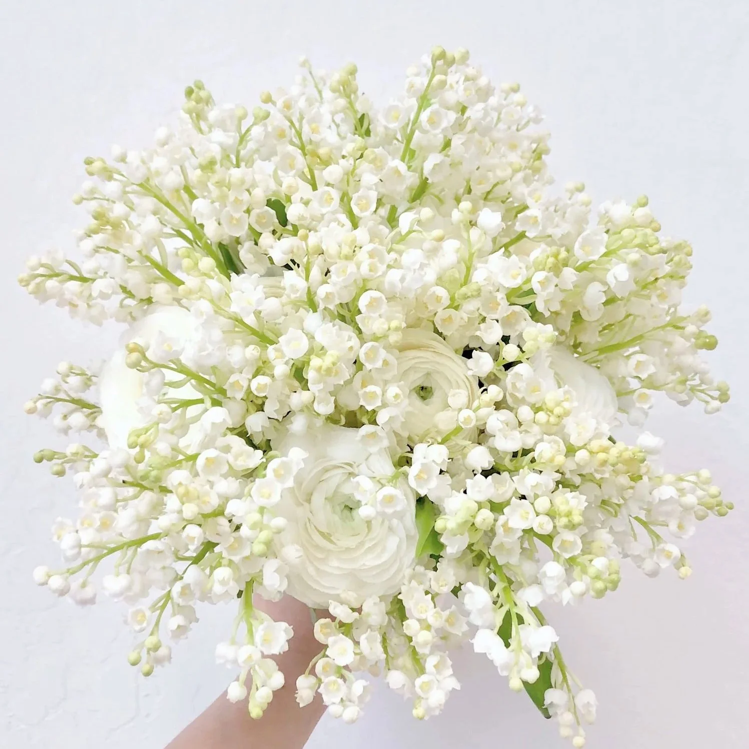 A bouquet of white flowers, including small bell-shaped blossoms and roses, held by a hand against a white background.