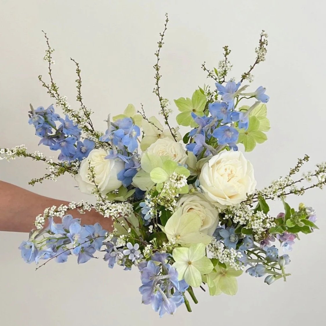 Bouquet of white roses, light blue delphiniums, and small white flowers with greenery.