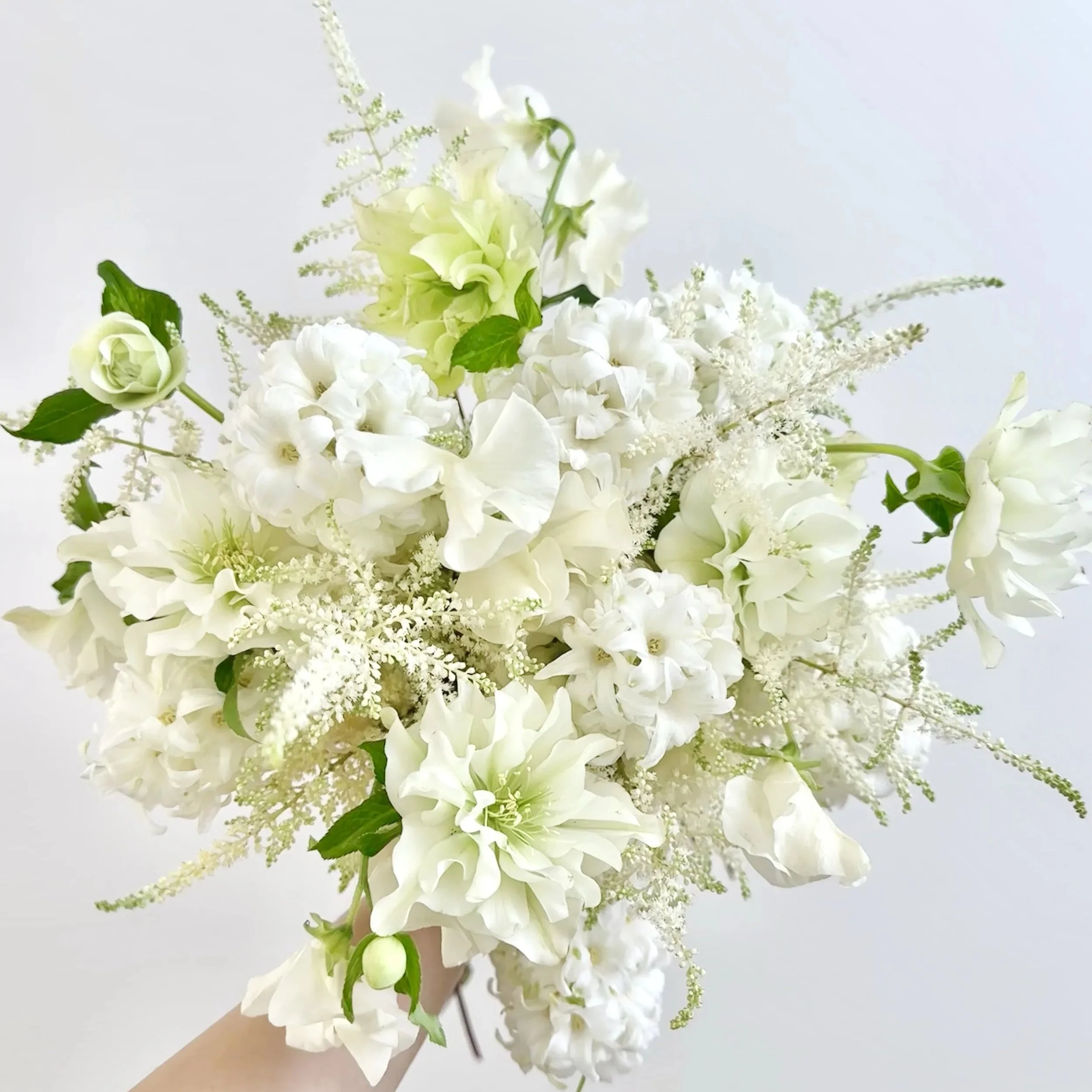 A person holding a bouquet of white and green flowers against a plain gray background.