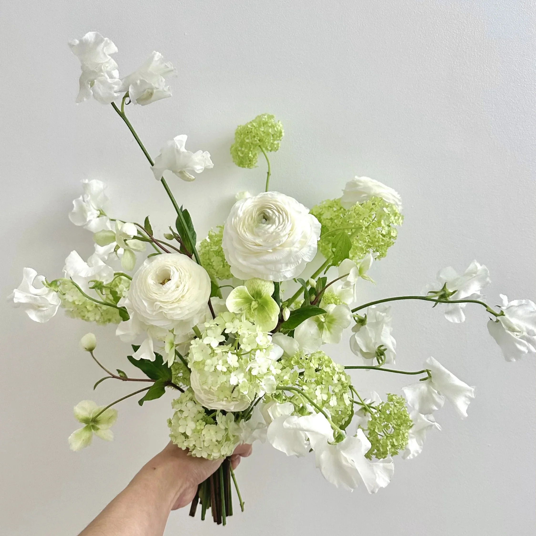 A hand holding a bouquet of white and green flowers against a plain background.