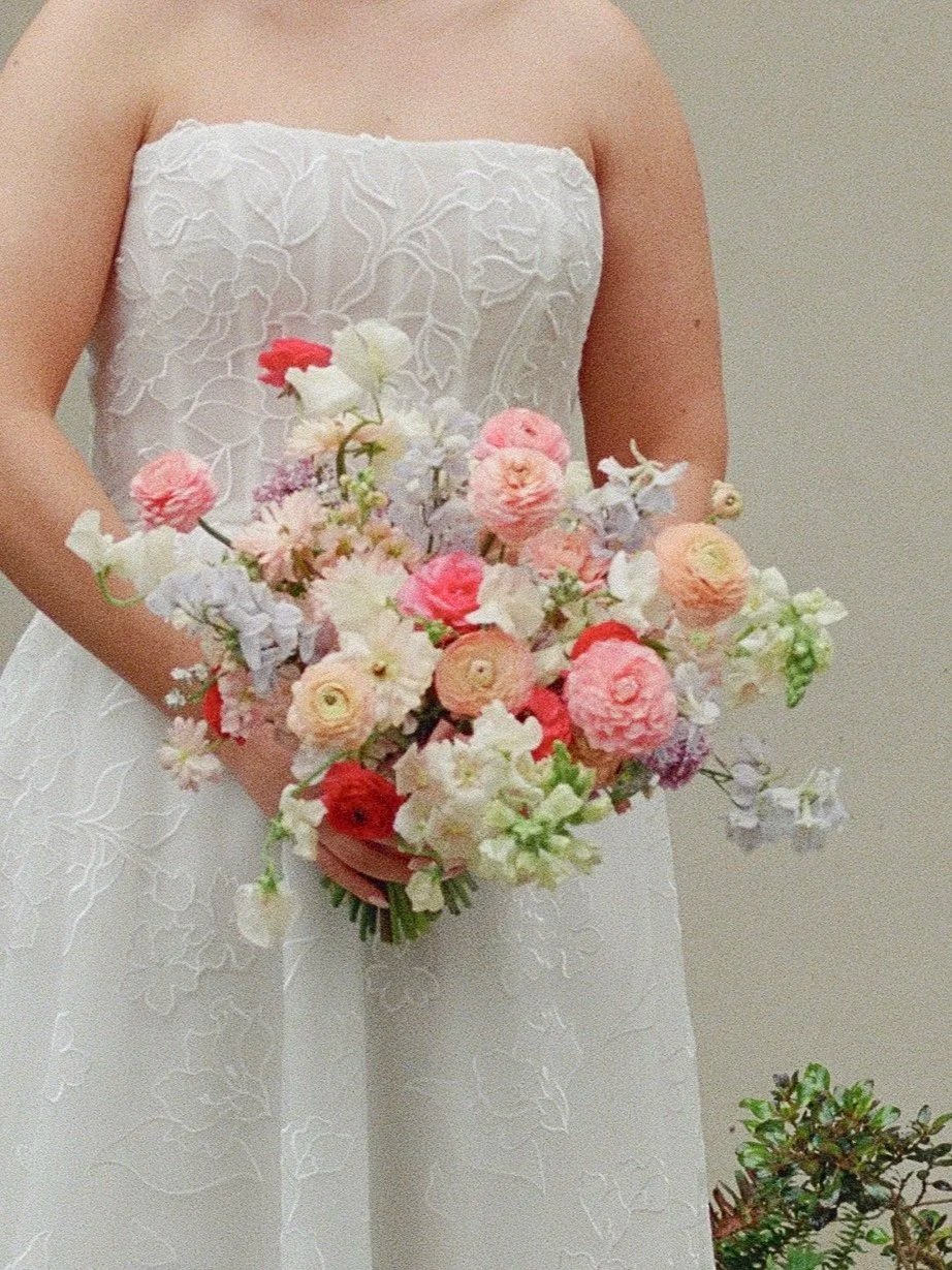 A woman in a white dress holding a bouquet of pink, white, and peach flowers.