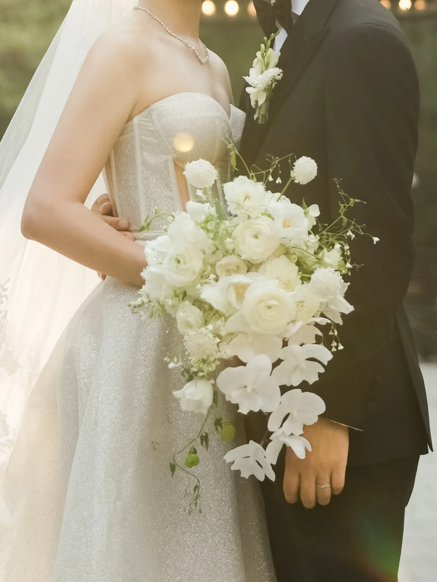 A bride and groom holding a bouquet of white flowers during their wedding ceremony or photoshoot.