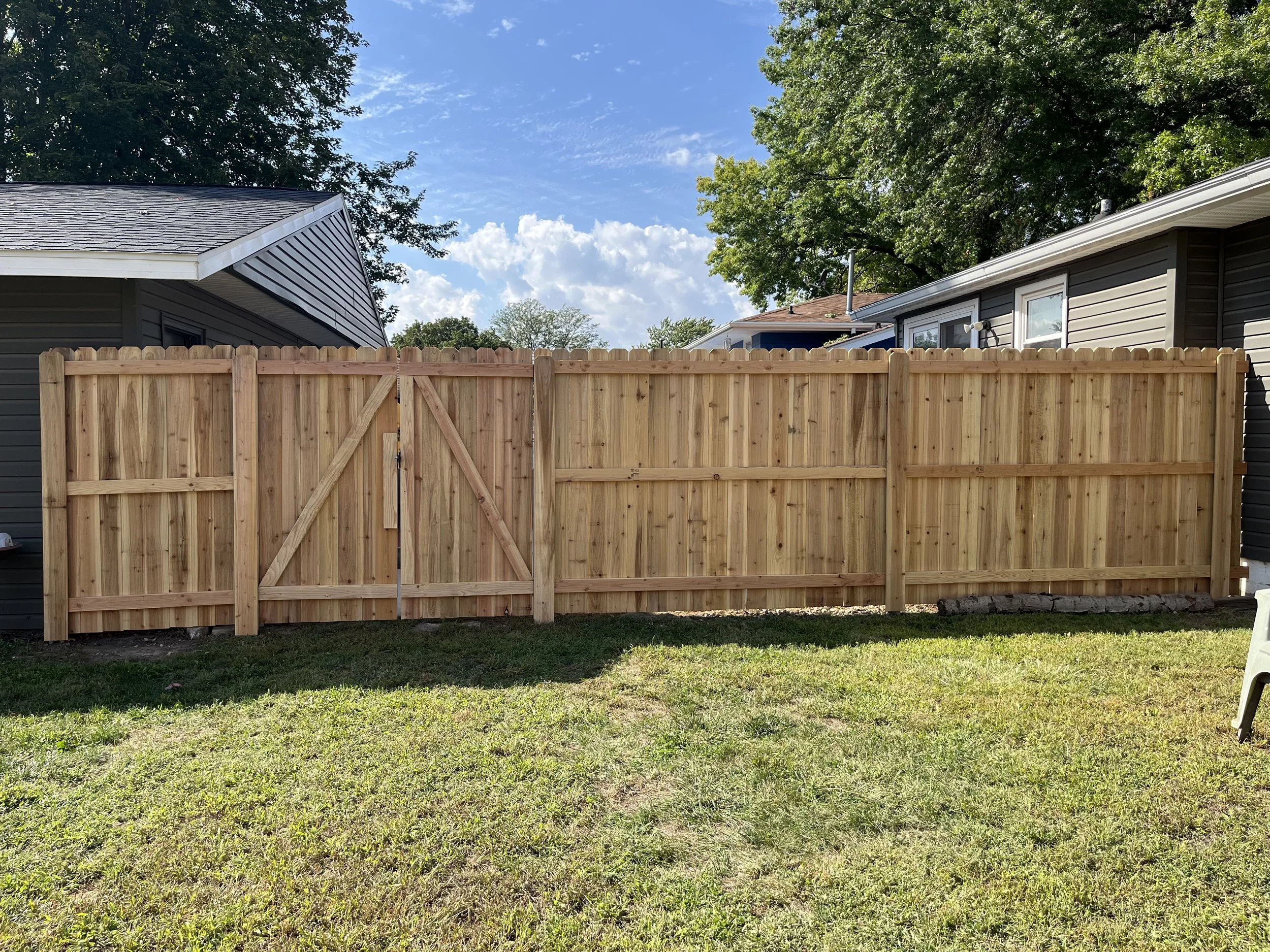 6-foot cedar privacy fence installed in a residential backyard, complete with a 6-foot double drive gate braced with custom on-site compression braces. The installation blends into the yard with grass and a patio visible, providing privacy with a cle
